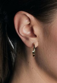 Złota kolczyk w kształcie hoop z gładką, błyszczącą powierzchnią, okrągłym kształtem i subtelną przerwą w projekcie, noszony na standardowym uchu.