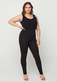 Débardeur noir associé à des leggings noirs. Le débardeur a une encolure ronde et les leggings présentent une taille sans couture et une coupe ajustée.
