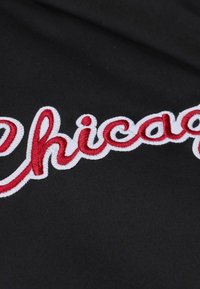 Schwarzer Stoff mit dem auffälligen roten gestickten Wort "Chicago", umrandet von Weiß. Glatte Textur mit klaren Nähdetails.