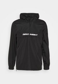 Zwarte pullover jas met capuchon, gemaakt van lichtgewicht materiaal, met elastische manchetten, een rits aan de voorkant en het "NIGHT ADDICT"-logo in witte letters over de borst.