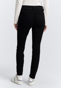 Sorte slim-fit jeans laget av denim, med middels høy midje, baklommer og en jevn tekstur. Brukt sammen med hvite sneakers.