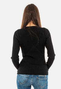 Top a maniche lunghe nero a coste con scollo rotondo e silhouette aderente, abbinato a jeans blu chiaro con tasche posteriori e cerniere.