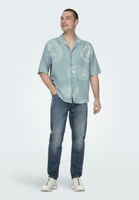 Kurzärmliges, hellblaues Hemd mit Paisleymuster, kombiniert mit blauen Jeans und weißen Sneakers. Lässiger Schnitt, mit Knopfleiste.