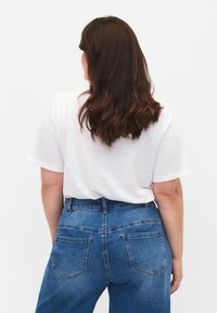 Witte T-shirt met korte mouwen gecombineerd met hoge taille blauwe spijkerbroeken. De spijkerbroeken hebben een gladde textuur en twee achterzakken.