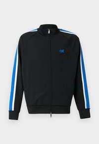 Veste de survêtement zippée noire avec un col montant, dotée de rayures bleues et blanches le long des manches et d'un petit logo bleu sur la poitrine.