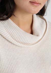 Cremefarbener, gestrickter Pullover mit weitem, Wasserfallausschnitt und strukturierter Rippung, der ein weiches und gemütliches Material betont.