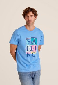 Lichtblauwe katoenen t-shirt met een kleurrijk zeilthema-graphic, voorzien van vetgedrukte tekst en een verscheidenheid aan kleuren. Rondek en korte mouwen.