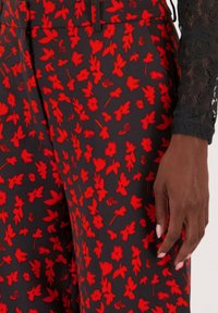 Bloemmotief broeken met een zwarte achtergrond en levendige rode bloemen. Gemaakt van gladde stof, met een comfortabele pasvorm en riemlussen.