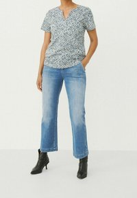 Bluse mit floralem Muster in Marineblau und Weiß, kombiniert mit hellblauen, kurzen Denim-Jeans und schwarzen, spitzen Ankle Boots.