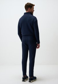 Survêtement bleu marine avec col montant et coupe ajustée, fabriqué en tissu doux. Dispose d'une poche à l'arrière des pantalons et de baskets.