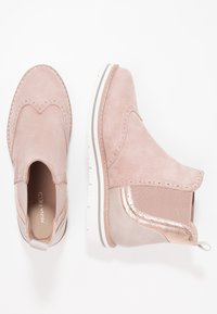 Růžové semišové kotníkové boty s brogue detaily, elastické boční panely, bílé podrážky se šedými pruhy a táhla na zadní straně.