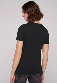 Camiseta negra ajustada hecha de una tela suave, con mangas cortas y un escote redondo clásico, vista desde la parte posterior. Detalles de costura sutiles.