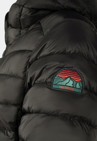 Czarna kurtka puchowa z pikowanymi sekcjami, błyszczącą teksturą oraz kolorowym haftowanym logo na lewym ramieniu przedstawiającym góry i zachód słońca.