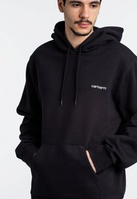 Sudadera de algodón negra con bolsillo frontal, capucha con cordón y pequeño logo blanco en el lado izquierdo del pecho. Diseño simple con puños de canalé.