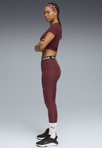Bordeaux atletisk crop top og højtaljede leggings med sort Puma-branding, parret med sorte sneakers og hvide ankelstrømper.