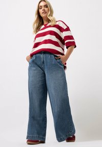 Rood-wit gestreepte oversized t-shirt met korte mouwen, gecombineerd met hoge taille, wijde blauwe jeans. Casual schoeisel zichtbaar.