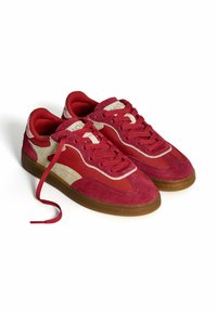 Red suede sneakers with beige leather accents. Rounded toe, lace-up front, padded collar, and gum rubber sole. One lace is untied.