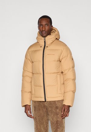 Beige színű puffert jaket, cipzáros zárással, kapucnival, steppelt mintázattal és oldalsó zsebekkel. A mellkason egy kis logó, a cipzáron pedig sötét díszítések találhatók.