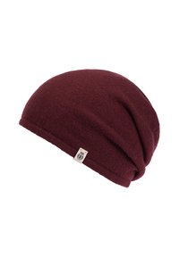 Burgundy knitted slouchy beanie with small beige logo tag featuring a black emblem on the folded edge.