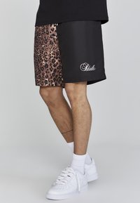 Pantaloni corti neri e con stampa leopardata, con una texture liscia, dotati di un logo bianco. Abbinati a sneakers bianche e calze corte.