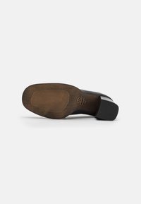 Suola di scarpe nera con un motivo testurizzato e scanalato. Finitura che ricorda il legno con punta arrotondata e tacco spesso e quadrato. Dettaglio sui bordi liscio.