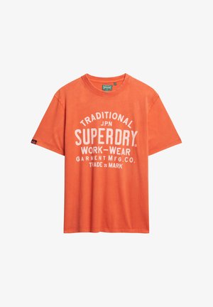 Oranje katoenen t-shirt met een ronde hals, korte mouwen en witte opdruk met de tekst "TRADITIONELE SUPERDRY WERKKLEDEN."