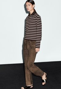 Camicia a maniche lunghe a righe marroni e bianche con colletto, abbinata a pantaloni scamosciati marroni e sandali in pelle nera. Superfici testurizzate e vestibilità casual.