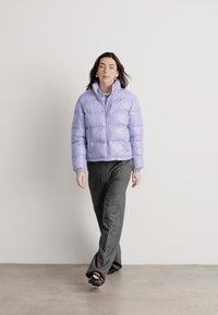 Chaqueta inflable lavanda con cierre de cremallera, puños acanalados y cuello alzado, combinada con pantalones de rayas grises. Textura suave y brillante.