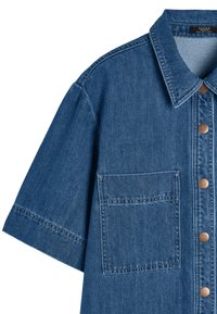 Koszula dżinsowa z wyraźnym kołnierzykiem, krótkimi rękawami i kieszonką z przodu. Jasnoniebieski kolor z brązowymi guzikami i widocznymi detalami ściegów.