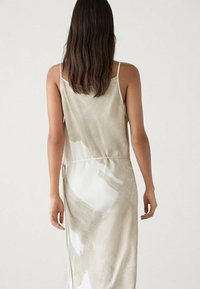 Robe sans manches beige avec des motifs abstraits blancs et marron clair, fabriquée en tissu doux, dotée d'une taille cintrée et d'une silhouette fluide.