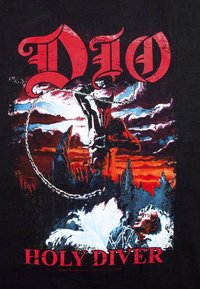 Svart bomull T-skjorte med et fargerikt grafisk motiv av en muskuløs figur med horn, kjeder og en skrikerfigur, merket "DIO HOLY DIVER."