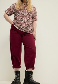 Lyhythihainen kuvioitu paita burgundin sävyissä, yhdistettynä löysiin burgundinvärisiin housuihin. Mustat nilkkurit, joissa on ketjuyksityiskohtia, täydentävät asua.