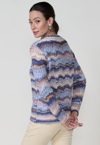 Pull en tricot avec un motif en zigzag dans des tons de bleu, rose et crème. Le tissu semble doux avec une finition texturée et un détail de poignet côtelé.