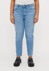 Hellblaue Denim-Jeans mit hoher Taille, geradem Schnitt, subtiler Ausbleichung und Fünf-Taschen-Design, kombiniert mit schwarzen, mit Nieten verzierten Slippern.