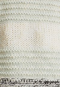 Tissu tricoté en menthe clair et crème avec des motifs texturés alternés. Le bas présente une fine rayure noire pour créer un contraste.