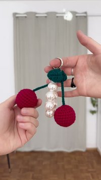 Klíčenka s dvěma červenými háčkovanými koulemi a skupinkou perlových korálků, vše připevněno k zelenému háčkovanému vršku s kovovým kroužkem.
