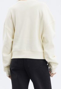 Roomwit oversized sweatshirts met verlaagde schouders, geribbelde halslijn en manchetten, gecombineerd met zwarte high-waisted jeans.