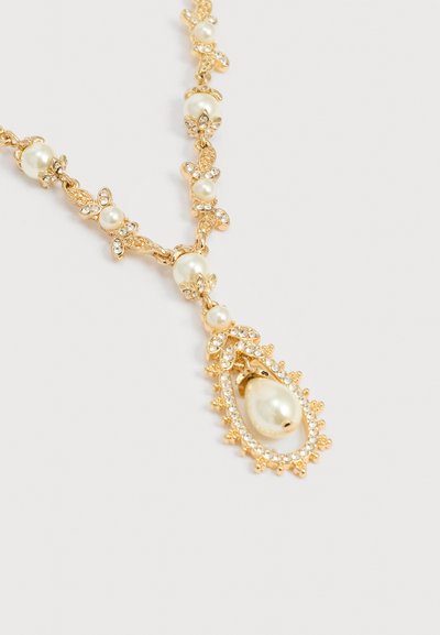 Κολιέ σε χρυσή απόχρωση με λευκές πέρλες, κρυστάλλινες λεπτομέρειες, λουλουδάτα μοτίβα και λευκή πέρλα σε σχήμα σταγόνας, σε απλό φόντο.