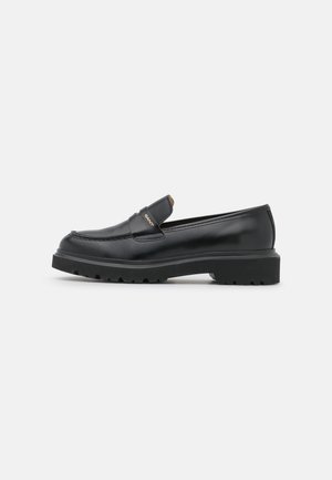 Mocassin noir en cuir avec semelle épaisse en caoutchouc et petit talon, avec un bout moc cousu et un petit logo doré "GANT" sur la bride.