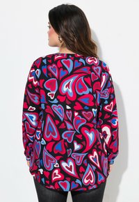 Langærmet bluse med et livligt hjerteprint i rød, blå og hvid på en sort baggrund, med en løs pasform og rundet kant.