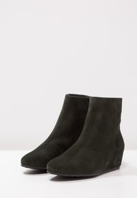 Bottines à talons compensés en daim vert foncé avec une texture lisse, un bout rond et un design élégant. Semelle extérieure noire plate pour la stabilité et le confort.