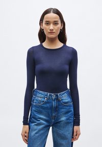 Body de manga larga de color azul marino hecho de material transparente, con cuello redondo y diseño ajustado, combinado con vaqueros azules de cintura alta.