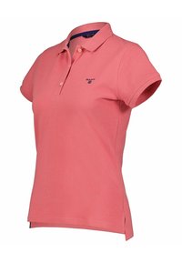 Růžová polo košile vyrobená z bavlny s krátkými rukávy, zapínáním na dva knoflíky a bočními rozparky. Obsahuje malé námořnické logo na hrudi.