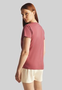 T-shirt rosa in morbido cotone con maniche corte e scollatura rotonda, abbinato a pantaloni corti chiari. Vista posteriore.