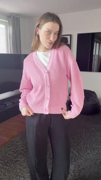 Ροζ ριμπ πλεκτή ζακέτα με V λαιμόκοψη, πέντε κουμπιά και μακριά μανίκια, συνδυασμένη με μαύρο παντελόνι. Πλεκτό ύφασμα με υφή και άνετη εφαρμογή.