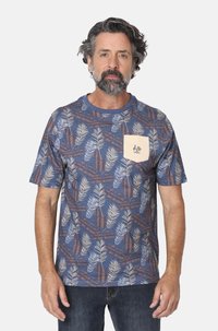 Camiseta de manga corta azul con un patrón de hojas en blanco y marrón. Presenta un bolsillo en el pecho de color crema con un detalle de marca.