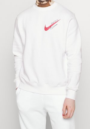 Vit crewneck-tröja i mjukt tyg. Har en röd Nike-logga och texten "Just do it." med en avslappnad passform och ribbade ärmslut.