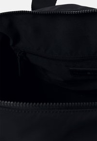 Interno di una borsa nera in nylon con una tasca con zip. Texture liscia, design minimalista e un'etichetta visibile vicino al bordo della tasca.