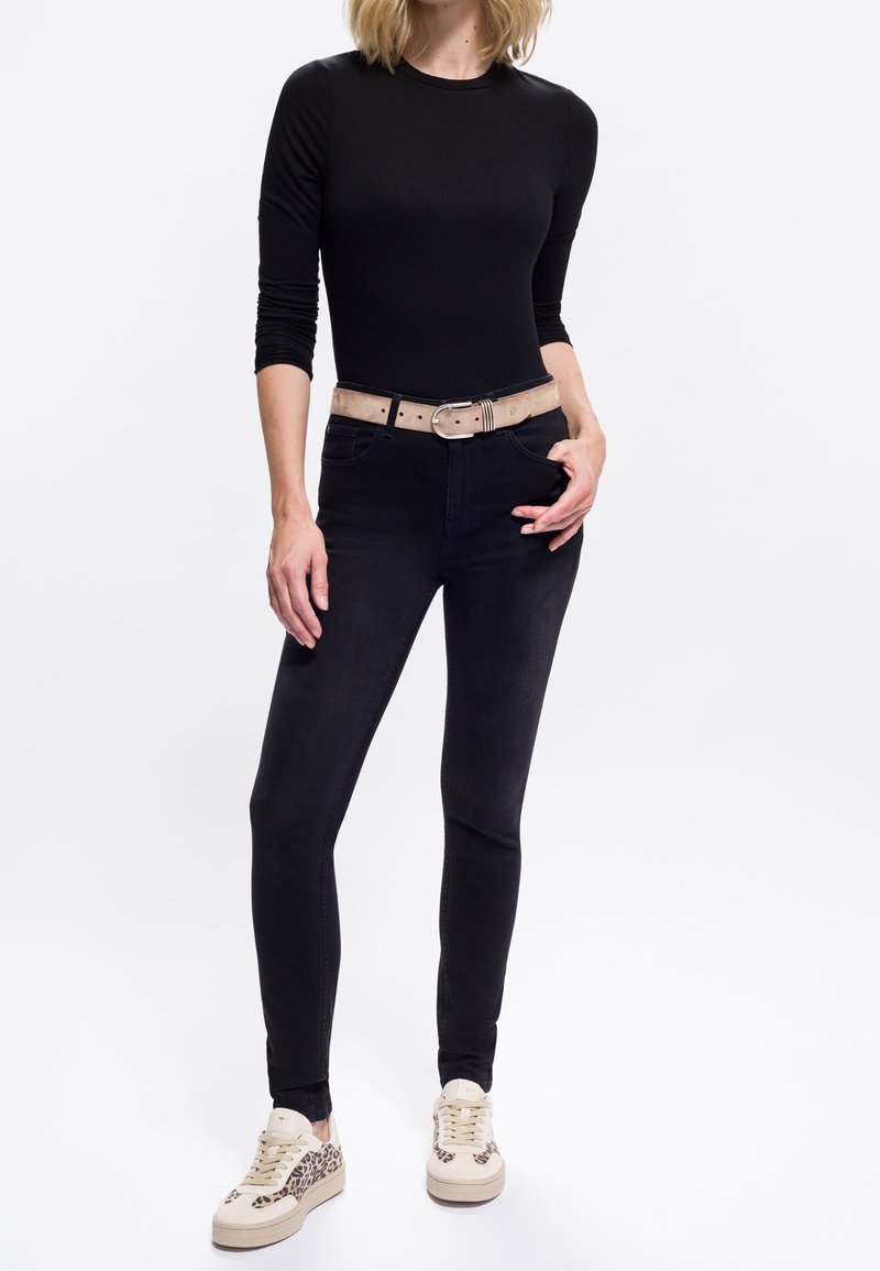 Maglietta nera a maniche lunghe, jeans neri a vita alta, cintura beige e sneakers beige con dettagli in stampa leopardata. Design semplice e aderente.