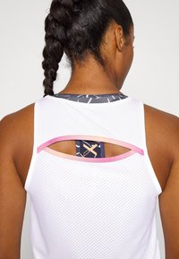 Canottiera atletica bianca con texture in rete, accenti rosa e blu navy, e una schiena scoperta che rivela un tessuto a fantasia sotto.